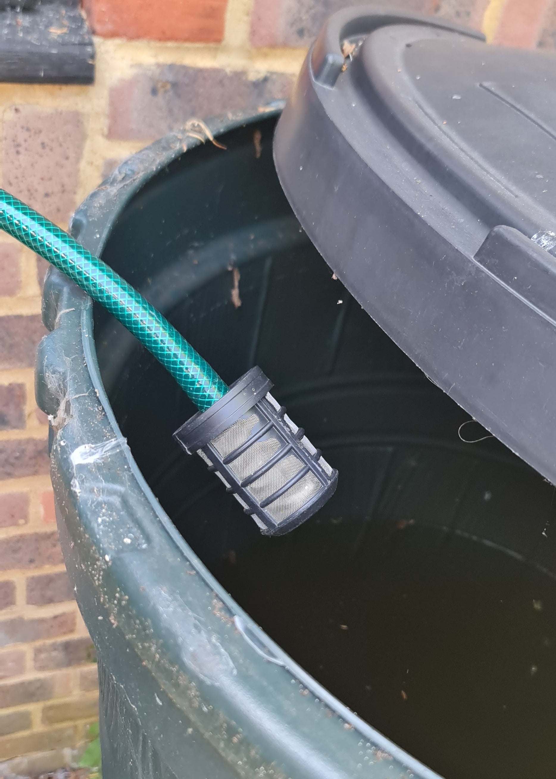 Submersible filter with a green garden hose attached, against on a brick wall.