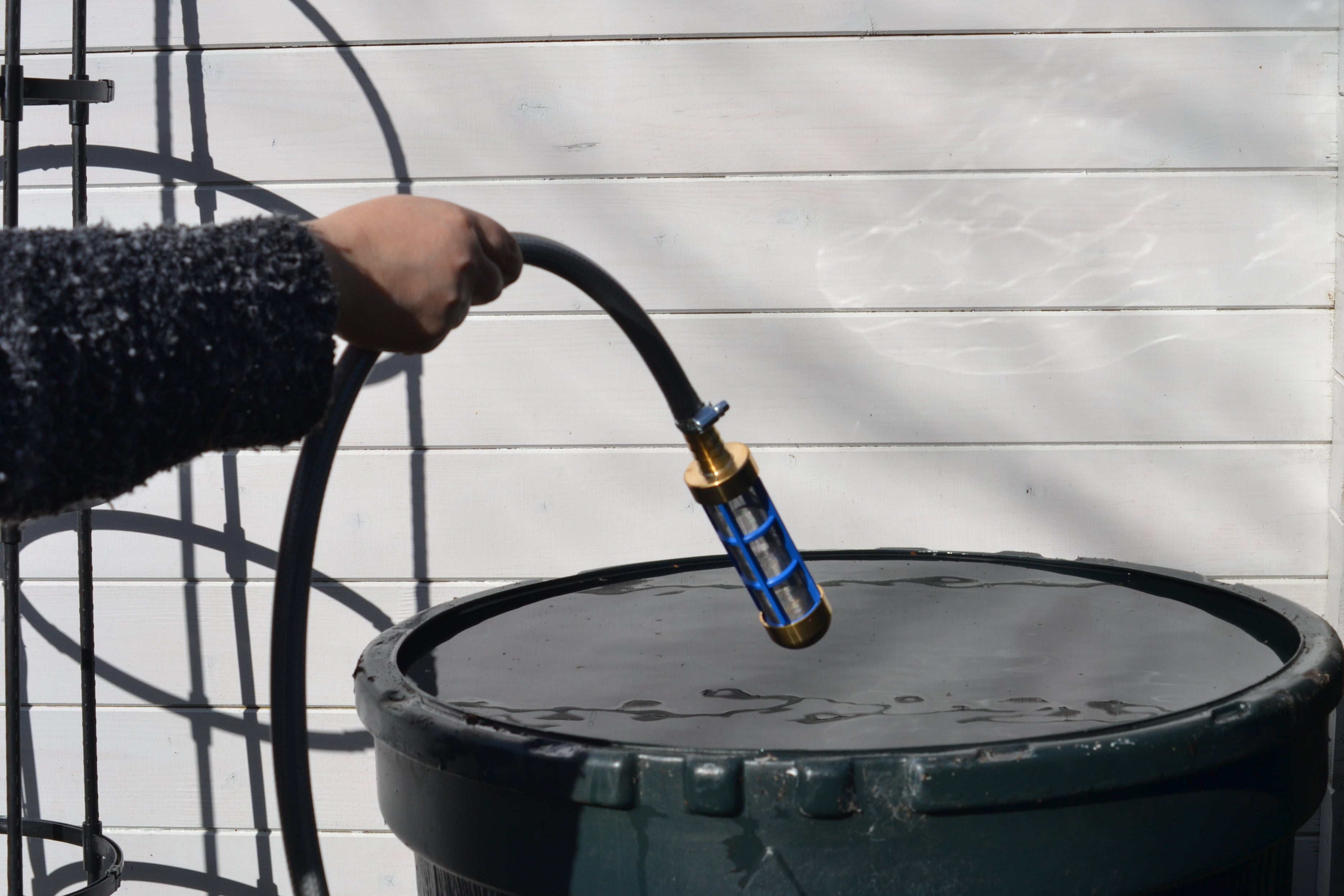 Person placing a brass submersible filter into the op of a rainwater barrel, in front of a white background