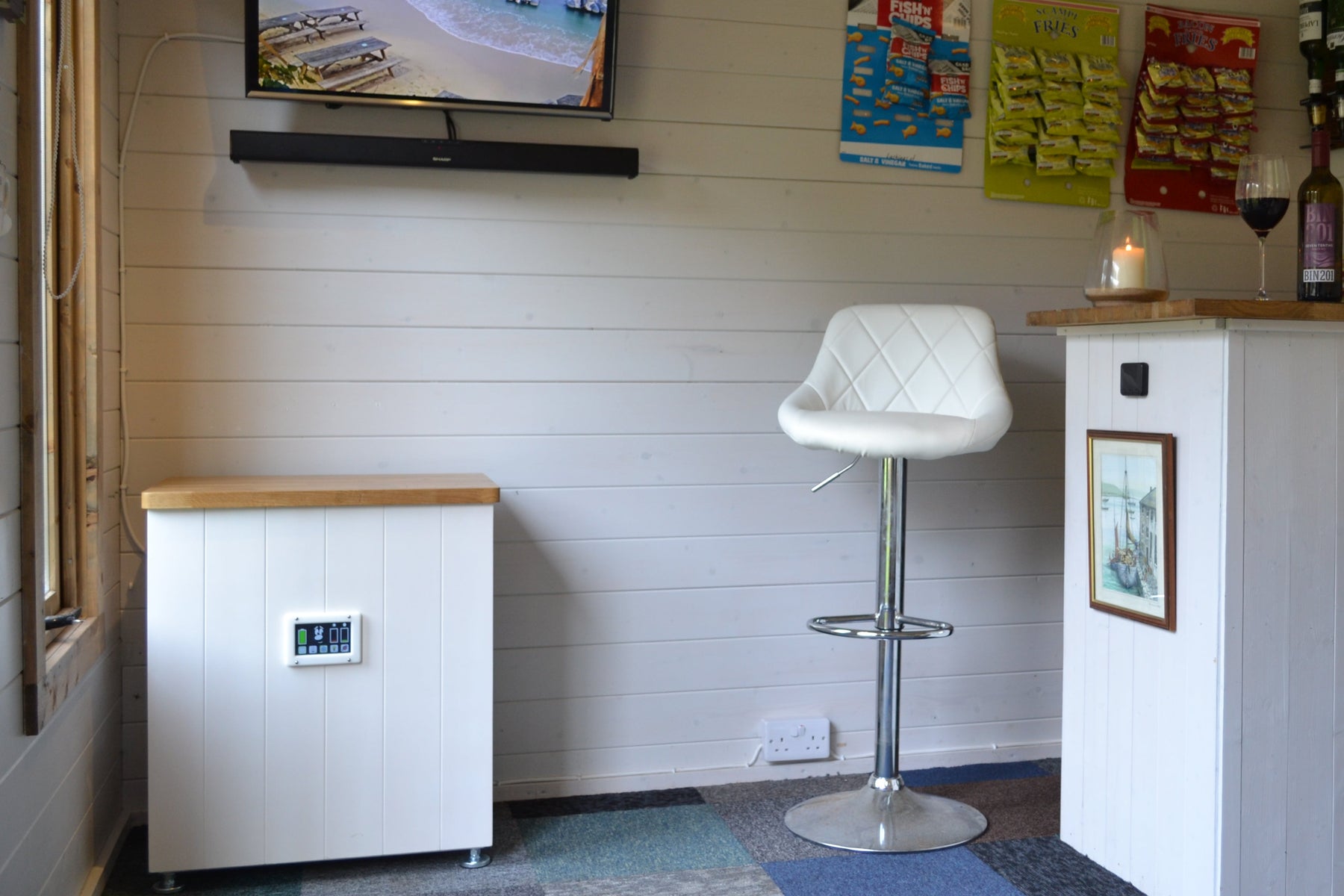 Small bar area with a television, and solar generator to poower it all, stools, and various items on shelves