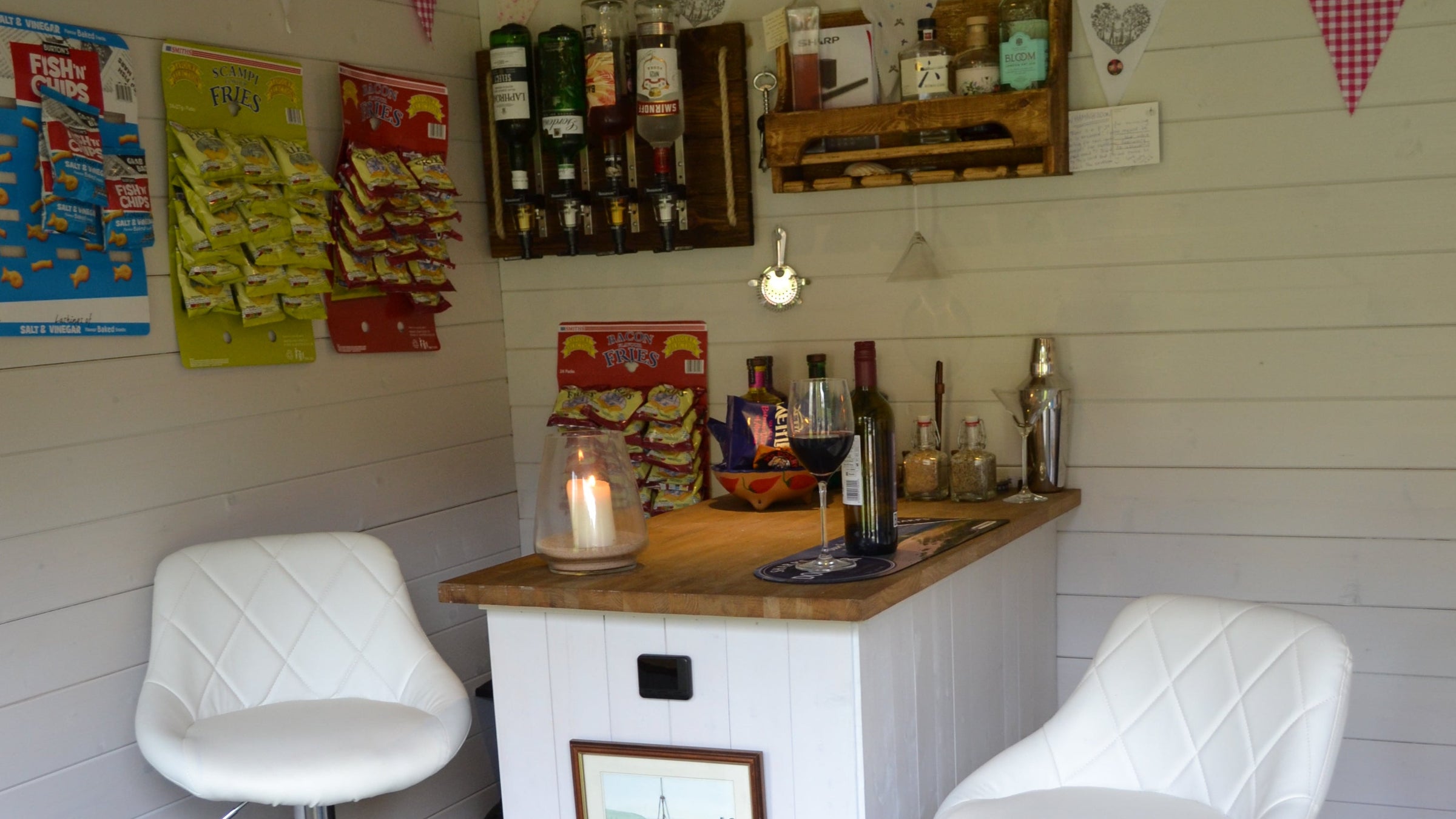 Small bar with chairs, and various items on shelves.ottles of alcohol and bar snacks on display. 